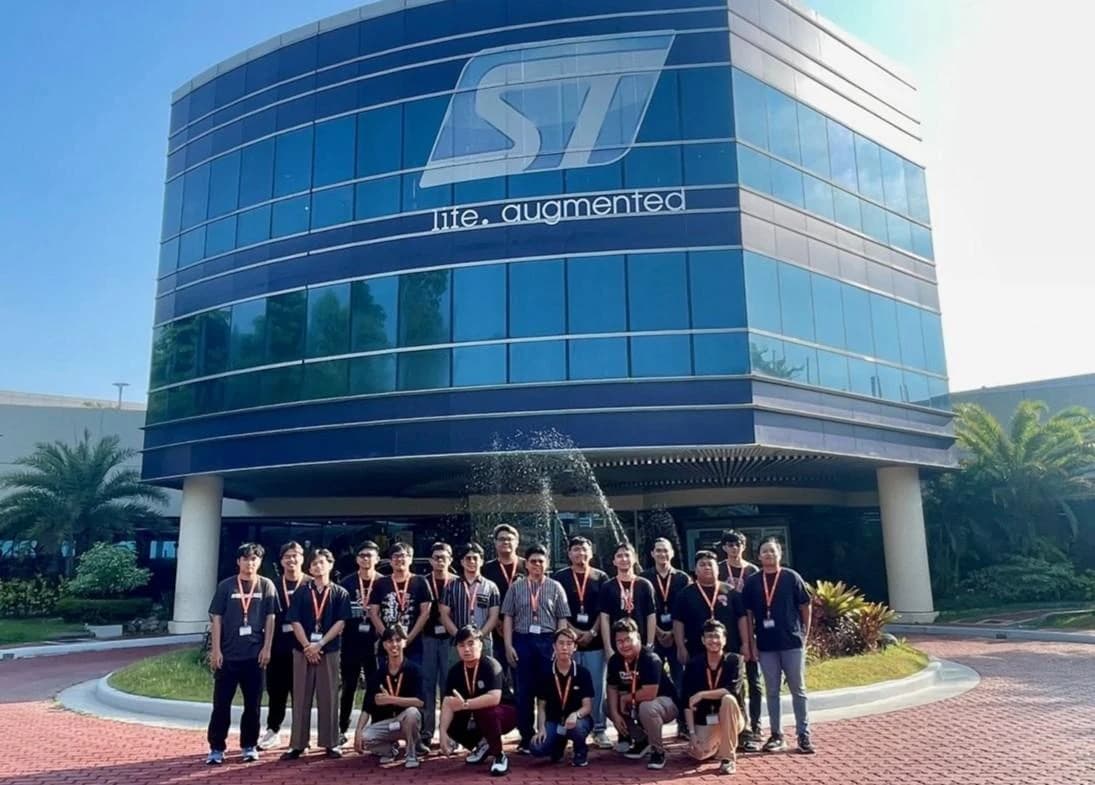 Group posing outside the STMicroelectronics building, below the ST logo.